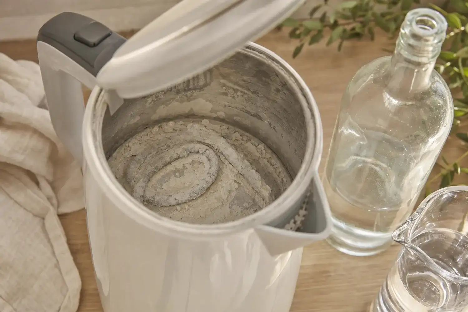 Fond et résistance d'une bouilloire couverts d'une croûte de tartre blanc, une bouteille de vinaigre blanc posée à côté