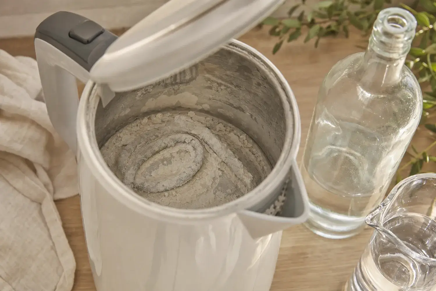 Fond et résistance d'une bouilloire couverts d'une croûte de tartre blanc, une bouteille de vinaigre blanc posée à côté